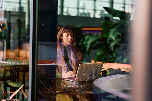 istock Woman working on laptop in cafe through window reflection 2247337397