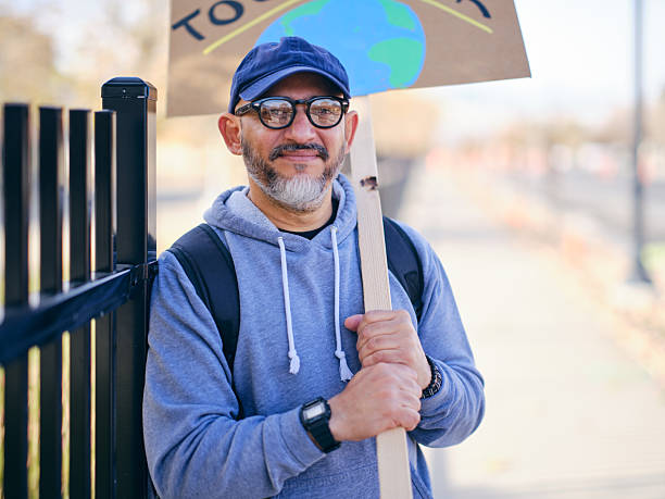 A portrait of a man at a community rally, holding a sign.