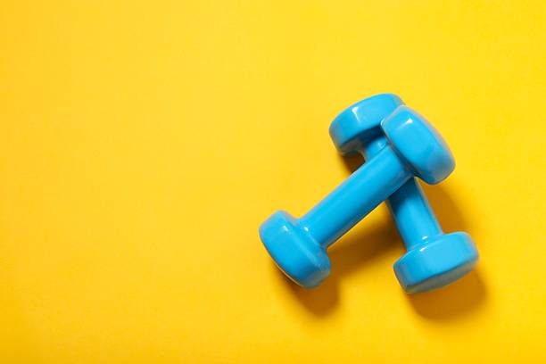 istock Two blue dumbbells isolated on yellow background, top view. Clipping-path, except the shadows, is included. 2247353737