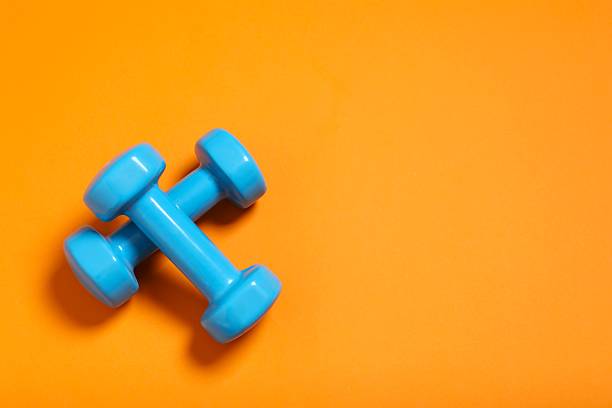 istock Fitness accessories concept. Blue dumbbells on orange background with copyspace 2247353828