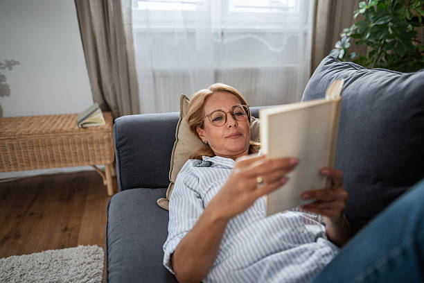 istock Mature woman relaxing on sofa reading book 2247354173