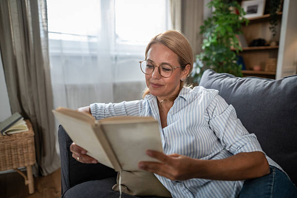 istock Mature woman relaxing on sofa reading a book 2247354200