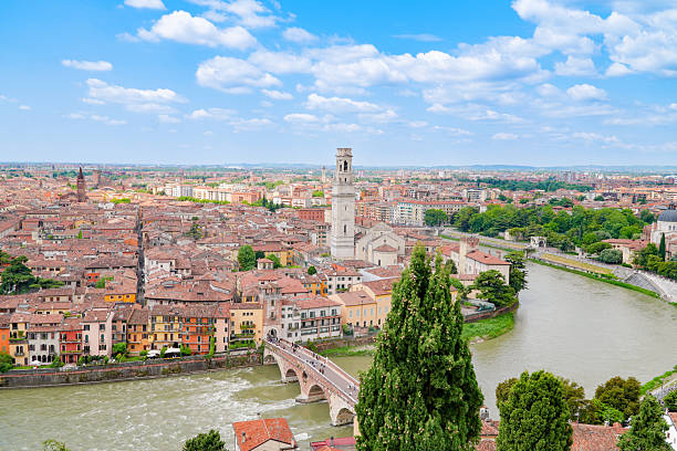 Panoramic photograph of the historic city of Verona, Italy, taken from the scenic viewpoint of Piazzale Castel San Pietro. The image captures the iconic cityscape with its terracotta rooftops, ancient bell towers, and the winding Adige River crossed by historic bridges like Ponte Pietra. This elevated view showcases the city's unique layout within the river's bend and its rich architectural heritage, making it one of the most beloved and romantic panoramas of this UNESCO World Heritage site.
