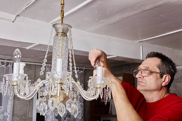 istock Removal process demonstrates technician taking out bulbs from crystal chandelier before lifting entire piece off ceiling in country home. 2247358022