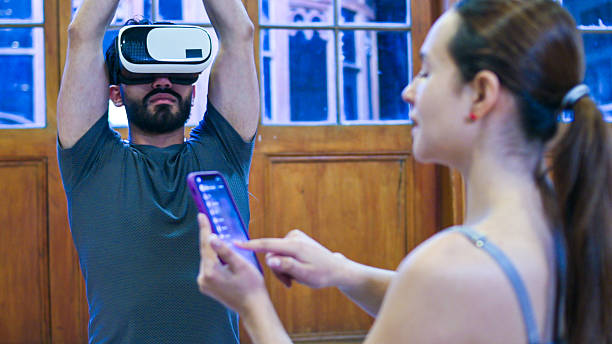 istock Man Wearing Virtual Reality Headset With Raised Hands While Woman Uses Smartphone Nearby 2247359010