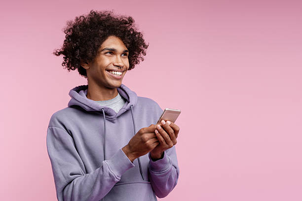 istock Smiling happy African American man holding mobile phone using mobile app text message looking away 2247362000