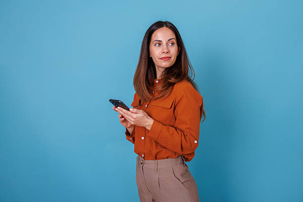 istock Woman holding smartphone and looking away, thinking about text message on blue studio background 2247363328