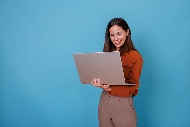 istock Young woman smiling, standing and using laptop, communicating online for business or education 2247365057