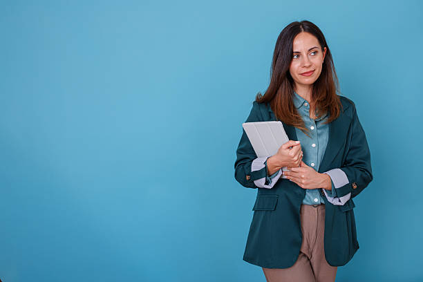 istock Businesswoman holding a white digital tablet, standing casually with folded arms, looking to the side with copy space 2247365556