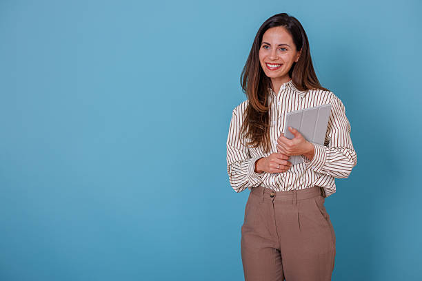 istock Smiling young female professional holding a tablet, posing in a studio setting with a blue backdrop and room for text 2247365913