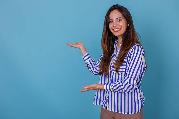 istock Smiling woman presenting copy space on blue background, gesturing with empty hands for advertisement 2247373095