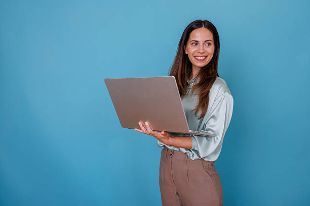 istock Professional woman smiling, looking away while holding laptop on blue background, concept of remote work and business communication 2247374296