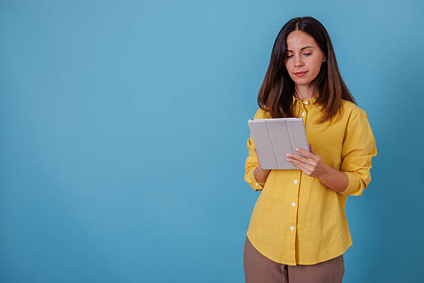 istock Young adult woman using digital tablet for remote work or online studying on blue background 2247374299