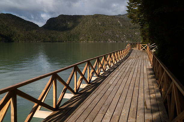 Wooden boardwalk extending over water with mountains and forest in caleta tortel, carretera austral, southern chile