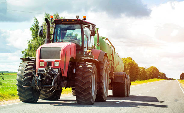 istock Red agricultural tractor with a semi-trailer with a barrel for transporting liquid fertilizers against the background of the sun and sky. Copy space for text, working 2247376168