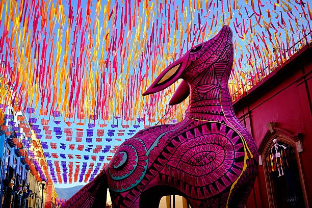 Oaxaca City, Oaxaca, Mexico – November 7, 2025: A pink alebrije stands beneath overlapping papel picado and streamers in vivid festival colors.