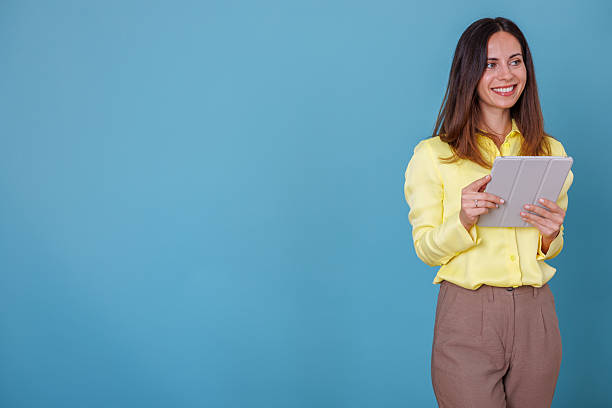 istock Woman using a digital tablet for business communication and remote work, standing against a blue background, smiling 2247377199