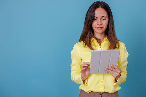 istock Woman wearing a bright yellow top is fully engrossed in her digital tablet, busy browsing, studying, or working remotely 2247377200