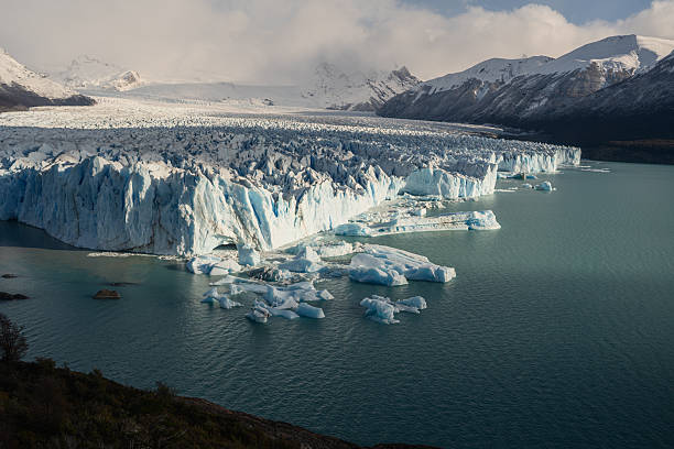 Perito moreno glacier showing pristine blue and white ice formation flowing into lake argentino with snow-capped mountains