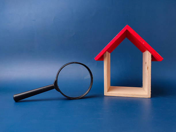 istock The image, featuring a small wooden house model and a magnifying glass on a blue background 2247379599