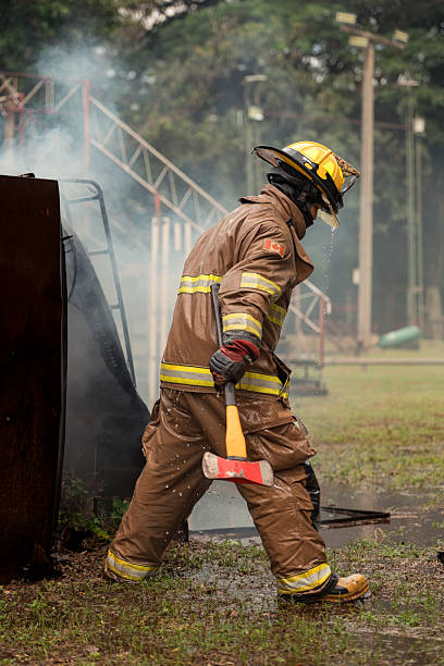 istock A firefighter in full turnout gear strikes a metal structure with a rescue axe during a live training drill. Water spray and smoke fill the scene 2247381007