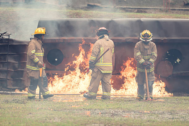 Firefighter bravely faces intense flames, standing firm in heavy protective gear as water spray surrounds.Moment captures courage, danger, and the high pressure of emergency fire response operations.