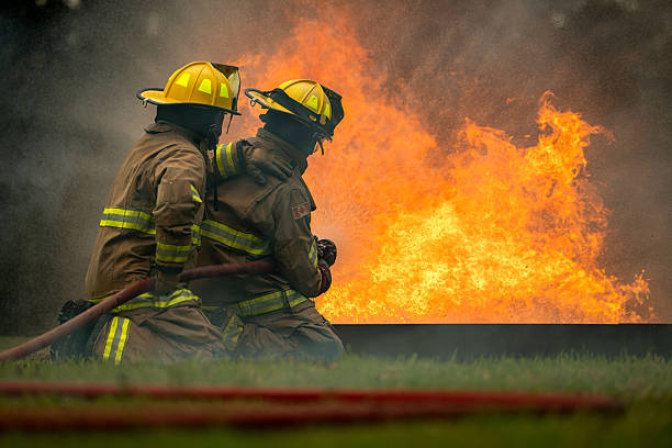 istock Two firefighters kneel in position while directing a powerful water stream at a large blaze 2247381481