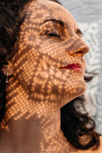 istock Woman with closed eyes, red lips, artistic leaf shadow on face, sunlight, peaceful moment 2247385140