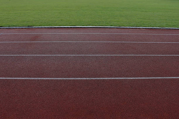 Red running track with white stripes markings at the stadium, green grass of the football field.