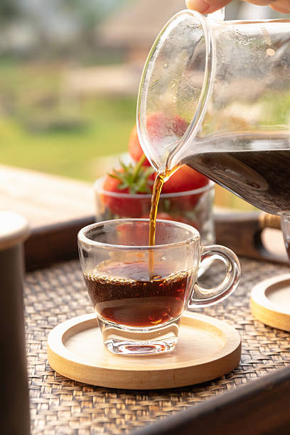 Pouring black coffee into glass cup on wooden coaster in morning patio, warm inviting beverage and fresh strawberries
