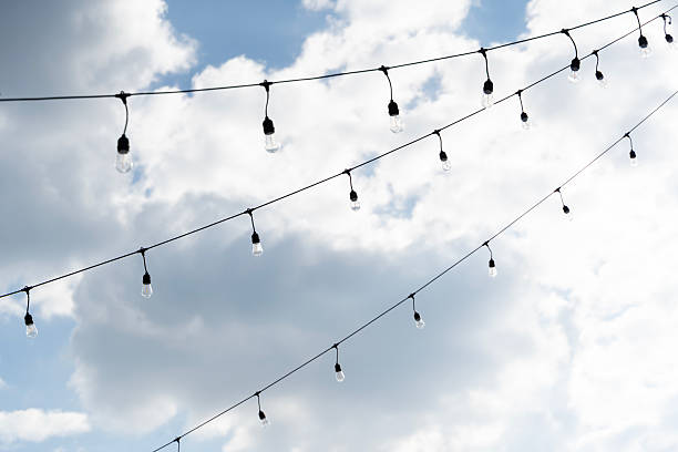 String lights hanging across an open sky with bright clouds, creating a minimal outdoor decoration mood suitable for events, celebrations, festivals, and peaceful ambient lighting concepts.