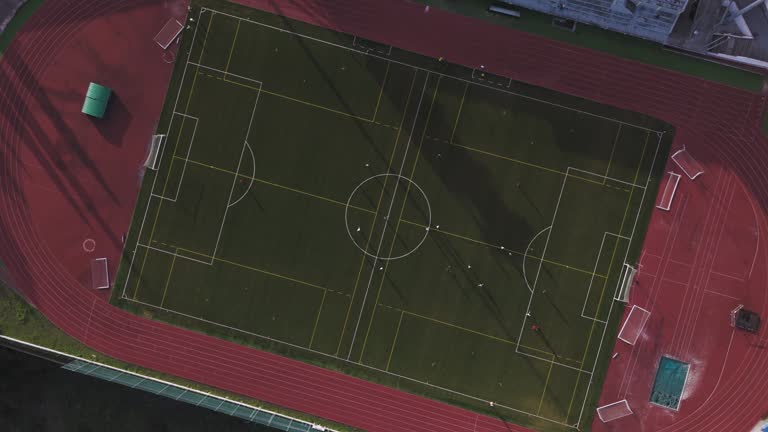 Top down drone shot over Monte da Galega stadium in Amadora Portugal showing soccer players on the field and the surrounding athletics track.
