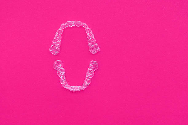 Clear aligners placed neatly on pink background, showcasing their transparent design and modern orthodontic technology. Clean minimal composition suitable for dental care and oral health themes
