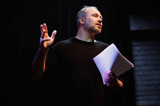 Performer in sweatshirt holding scenario in theater