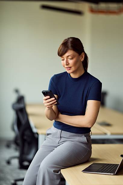 istock Professional Woman Using Smartphone At Modern Office Desk With Laptop In Quiet Workspace 2247415316