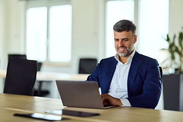 istock Confident Businessman in Blue Suit Working on Laptop in Modern Open Office Workspace 2247415324
