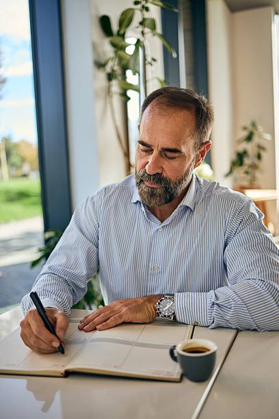 istock Professional Man Writing In Planner At Office Desk With Coffee Cup And Greenery Background 2247415351