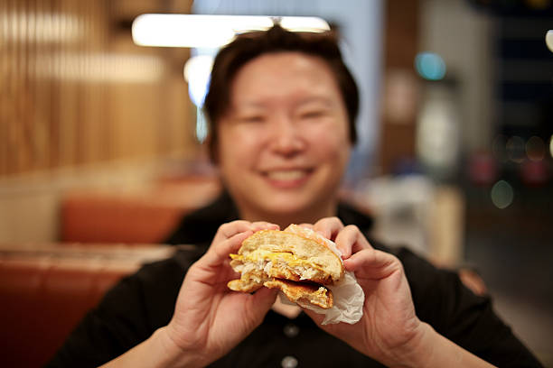An Asian woman is enjoying fast food (fish burger) for breakfast