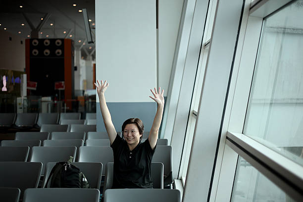 An Asian woman is waving cheerfully while seated at airport