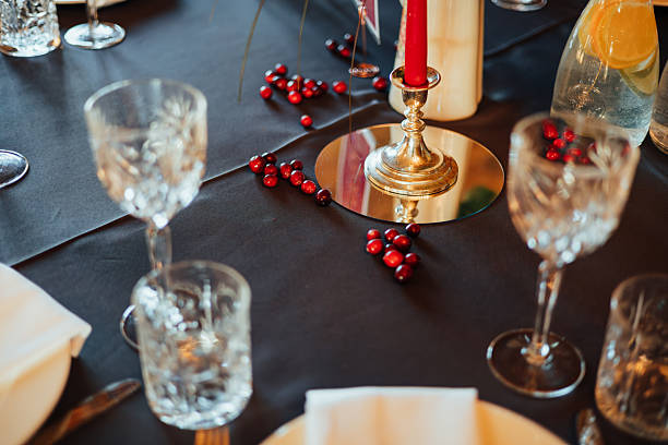 istock A festive table setup featuring crystal glasses, a red candle in a silver holder on a mirror, and scattered cranberries on a dark tablecloth. Lemon water pitcher in view 2247421324