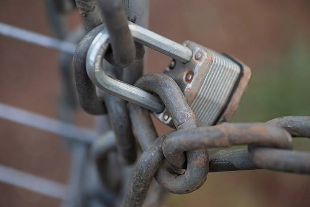 A mechanical lock with a bolt around a big chain and a metalic gate