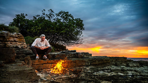 istock Man Meditating by Campfire on Rocky Cliffs at Sunset 2247427308