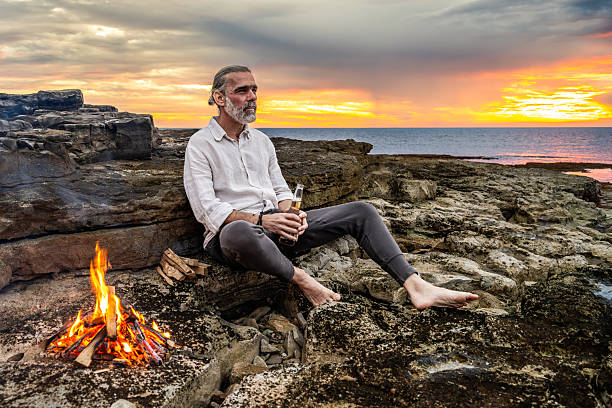 istock Man Sitting by Campfire Holding Drink at Sunset 2247427314