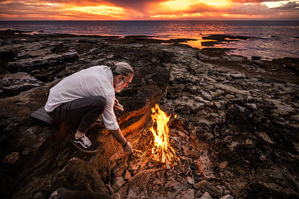 istock Person Crouching by Campfire on Rocky Terrain at Sunset 2247427318
