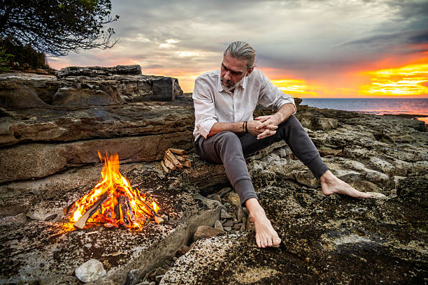 istock Man Sitting by Campfire at Sunset, Reflecting in Nature 2247427321