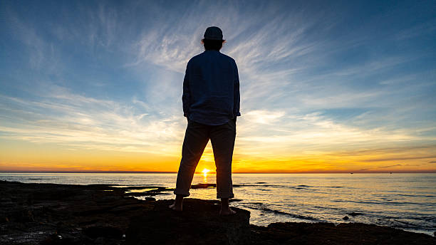istock Solitary Figure on Rocky Shore at Sunset 2247427326