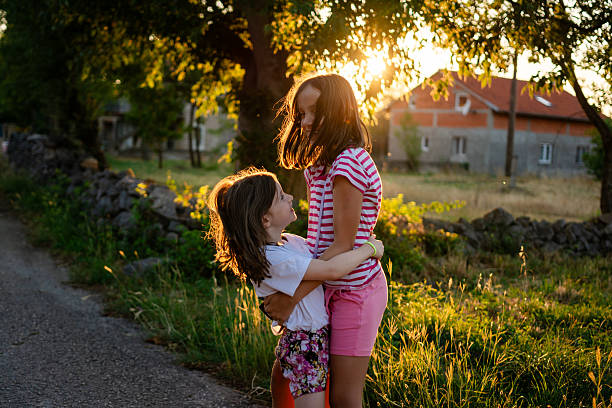 Two girls hugging and smiling on a rural road at sunset, capturing childhood joy, love, and family moments