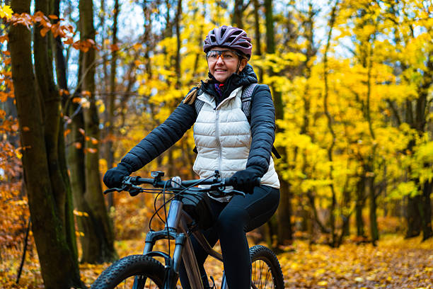 istock Middle-aged beautiful woman riding bicycle in forest in autumn. Front view 2247430190