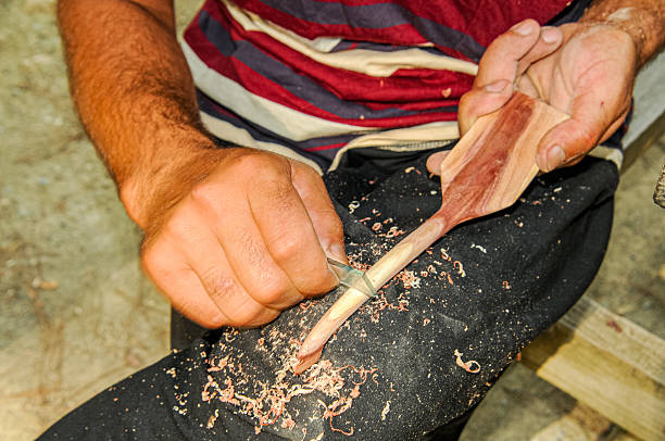 A man uses broken glass to make a wooden spoon
