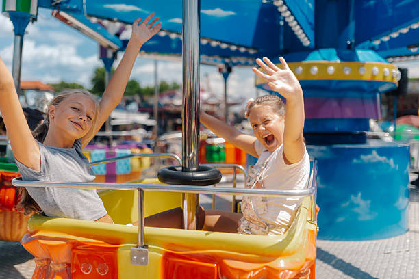 istock Two girls waving and having fun on a carousel ride at amusement park 2247432320